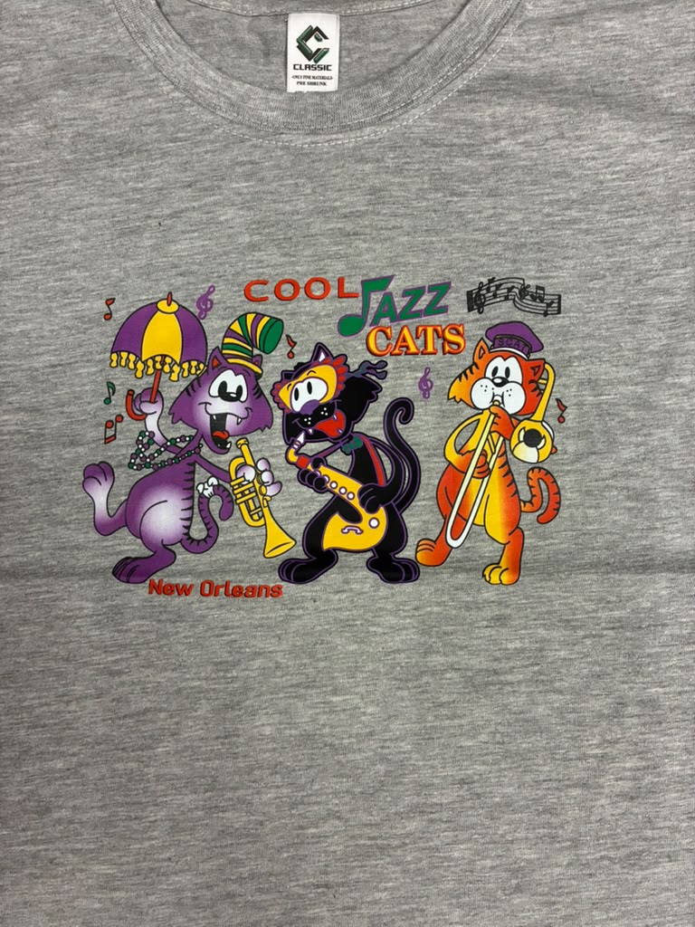 A close-up of a heather gray t-shirt featuring a colorful graphic of three cartoon cats playing jazz instruments under the text 'COOL JAZZ CATS' and 'New Orleans'. The neck label shows the brand 'Climax'.