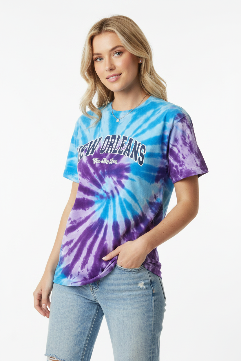 A woman modeling a short-sleeve tie-dye t-shirt with a blue and purple spiral pattern and 'New Orleans' printed across the chest, paired with light-wash jeans against a plain white background.
