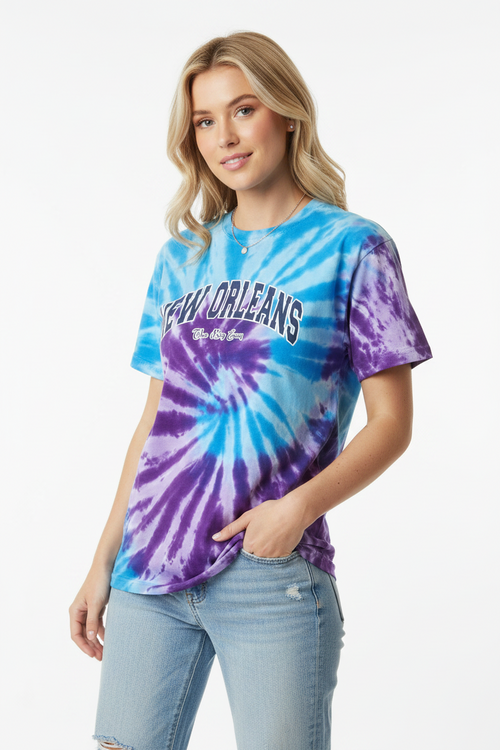 A woman modeling a short-sleeve tie-dye t-shirt with a blue and purple spiral pattern and 'New Orleans' printed across the chest, paired with light-wash jeans against a plain white background.