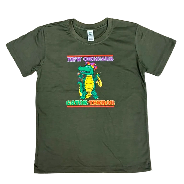An olive green short-sleeve t-shirt with a colorful graphic of the New Orleans 'Gator' mascot, featuring the text 'NEW ORLEANS' above and 'GATOR MASCOT' below, laid flat on a brown wood floor.