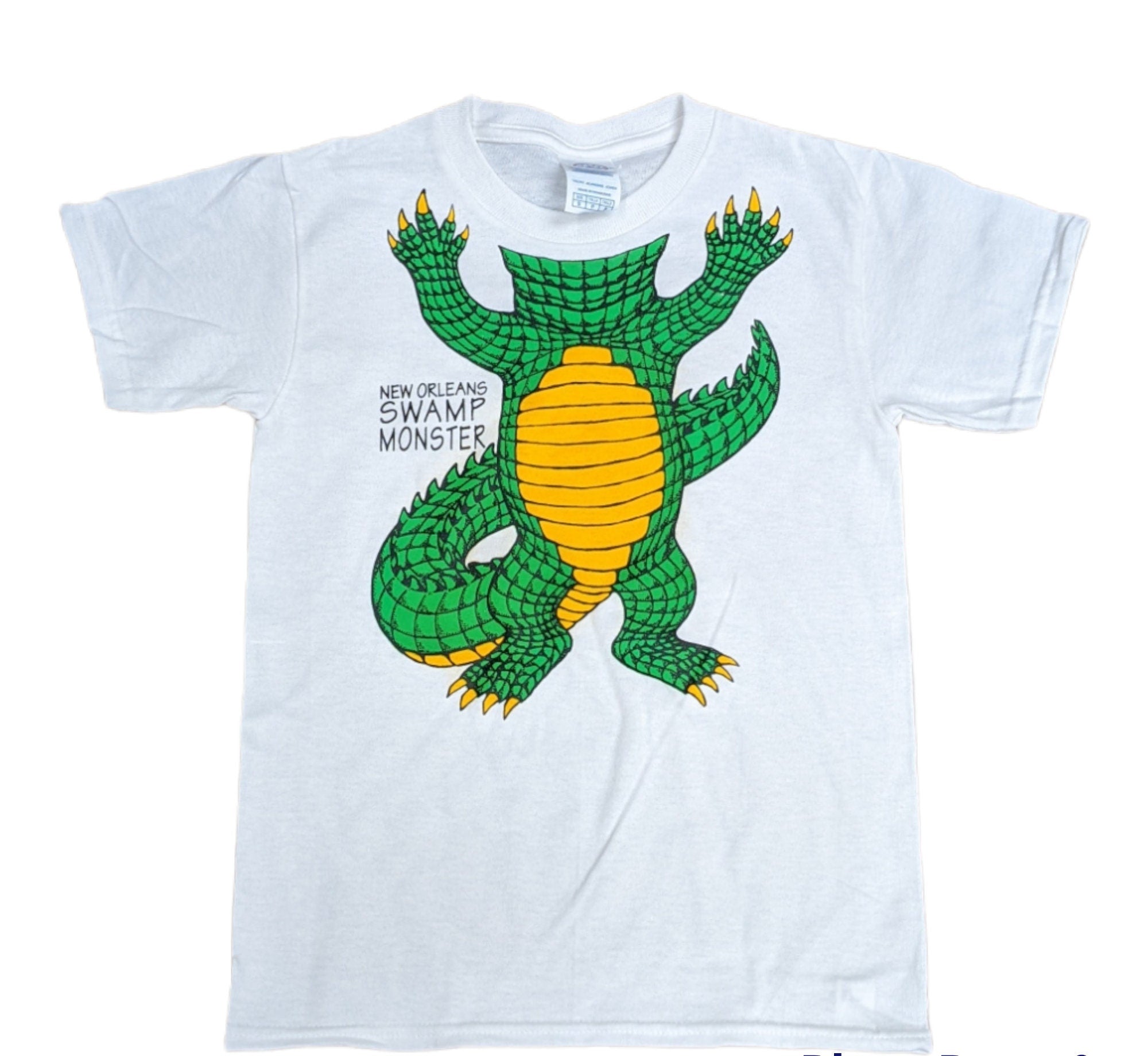 A white short-sleeve t-shirt featuring a colorful graphic of a green alligator with a yellow belly and black text that reads 'NEW ORLEANS SWAMP MONSTER'.