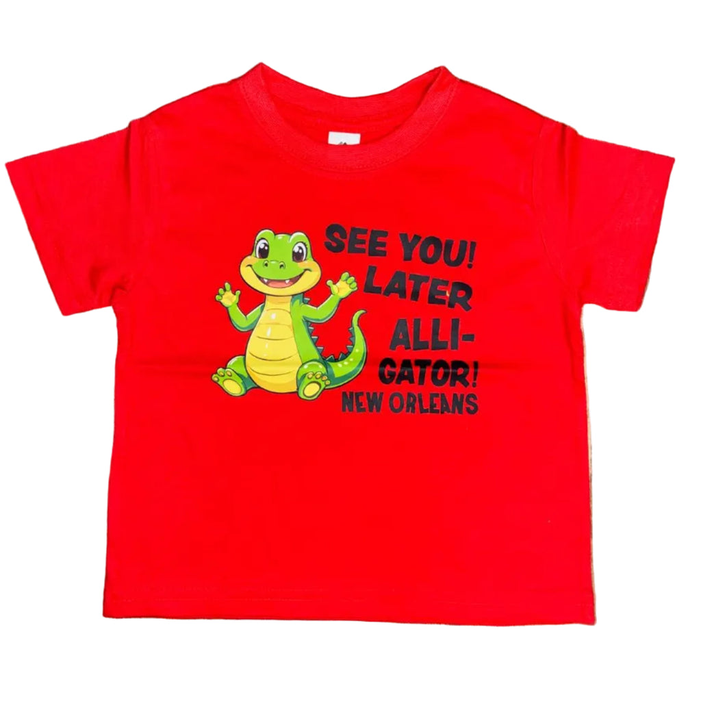 A bright red short-sleeve t-shirt laid flat on a white background. The shirt features a cartoon alligator graphic in green and yellow, alongside black text that reads 'SEE YOU LATER ALLI-GATOR' and 'NEW ORLEANS.'