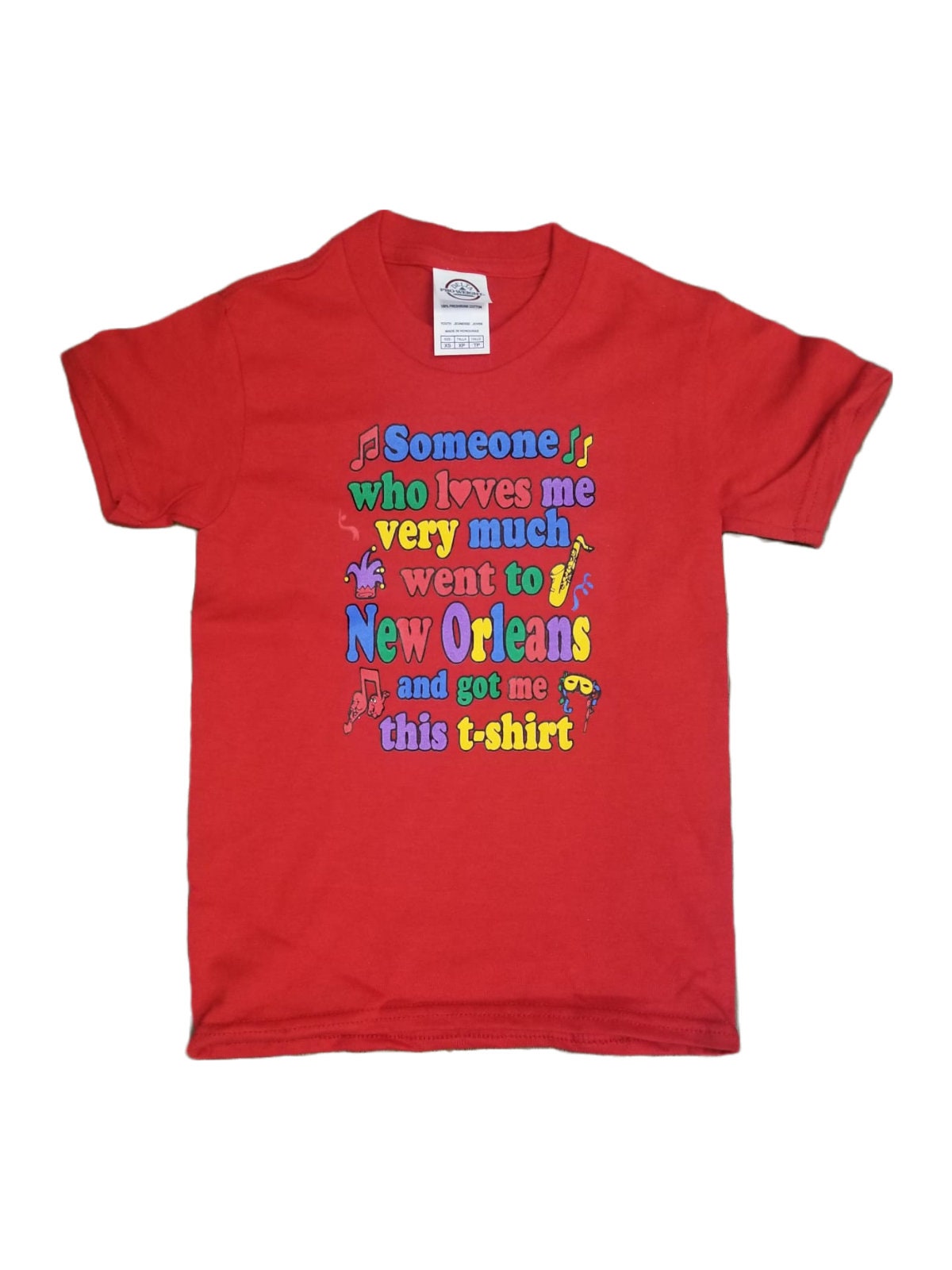 A red short-sleeve t-shirt with a colorful graphic text print on the front that reads 'Someone who loves me very much went to New Orleans and got me this t-shirt' accompanied by small musical notes and Mardi Gras beads.