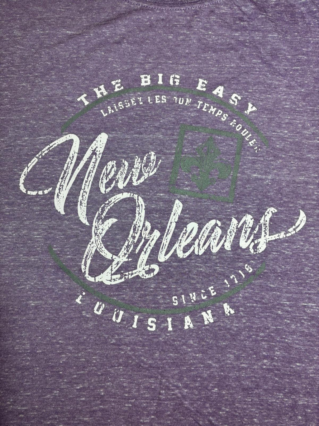 Close-up of heather purple t-shirt graphic featuring distressed white script 'New Orleans Louisiana Since 1718 The Big Easy' with fleur-de-lis detail in green"