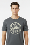 A man wearing a dark heather gray t-shirt with a distressed cream-colored circular graphic that reads 'THE BIG EASY NEW ORLEANS' and features a cityscape illustration in the center.