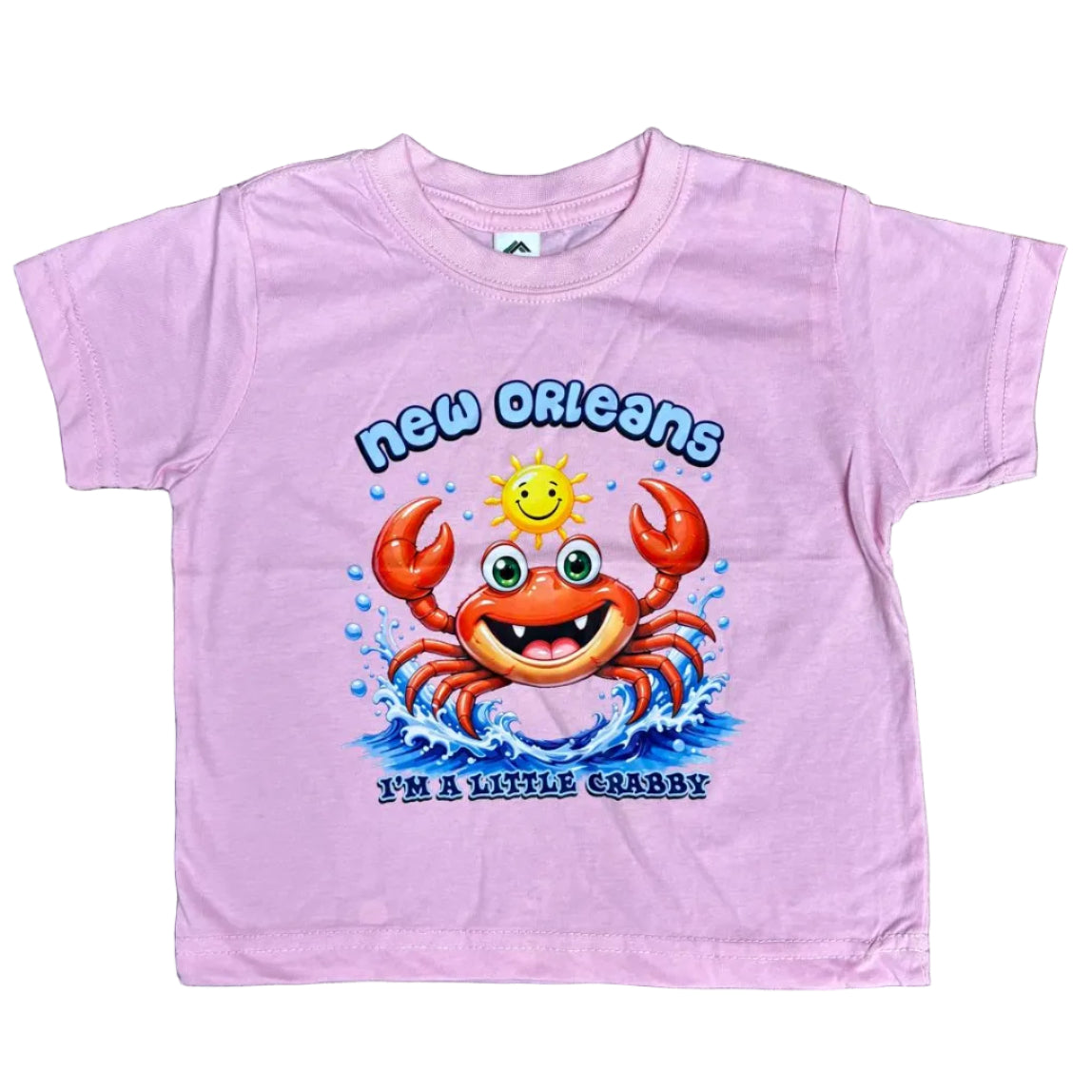 A light pink short-sleeve t-shirt laid flat on a white background, featuring a colorful graphic of a smiling orange-red crab, blue waves, and the text 'New Orleans' and 'I'm a little Crabby.'
