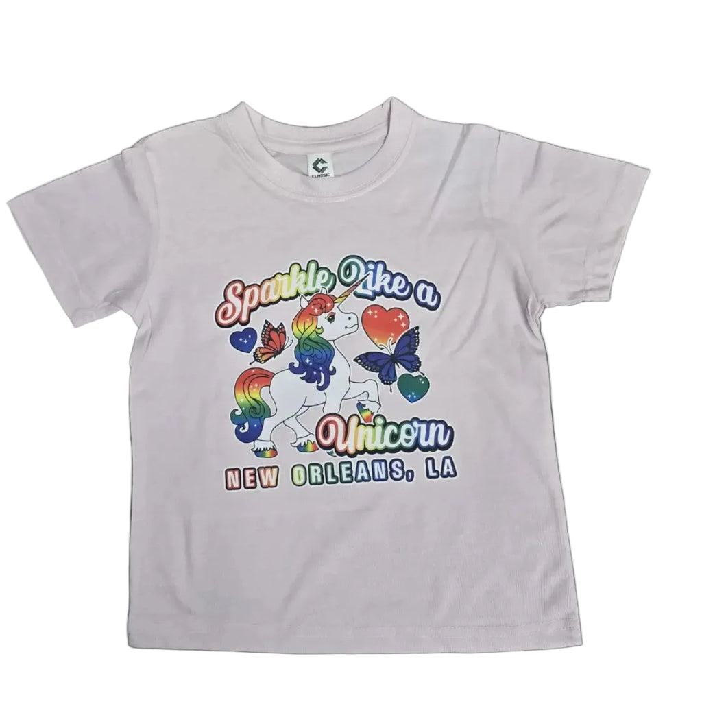 A pink short-sleeve kids' t-shirt with a colorful graphic of a unicorn, butterflies, and the text 'Sparkle Like a Unicorn NEW ORLEANS, LA', laid flat on a dark wood floor.