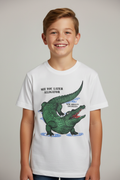 A smiling young boy wearing a white short-sleeve t-shirt with a green alligator graphic and the text 'SEE YOU LATER ALLIGATOR' and 'NEW ORLEANS, LA.' on a light gray studio background.