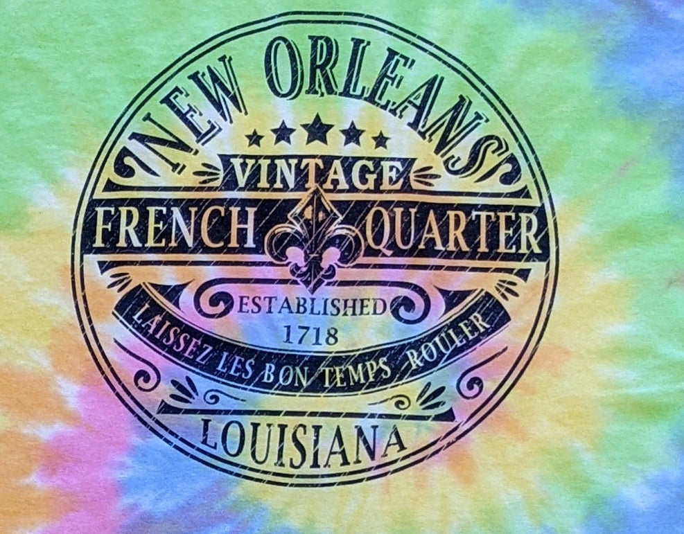 A short-sleeve crewneck t-shirt featuring a vibrant spiral tie-dye pattern in green, blue, pink, yellow, and orange. The center of the shirt is printed with a circular graphic that reads 'New Orleans Vintage French Quarter Louisiana'.