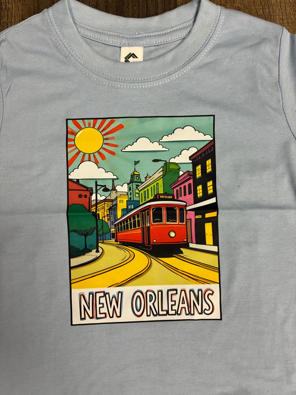 A light blue crewneck t-shirt featuring a colorful graphic print of a red streetcar on a yellow track with the text 'NEW ORLEANS' at the bottom.